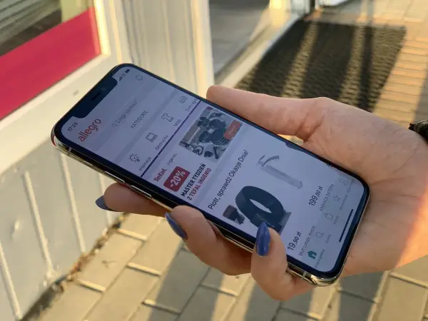 Dłoń trzyma iPhone 11, na ekranie aplikacja Allegro. Idealne iphone 11 wymiary do przeglądania ofert.