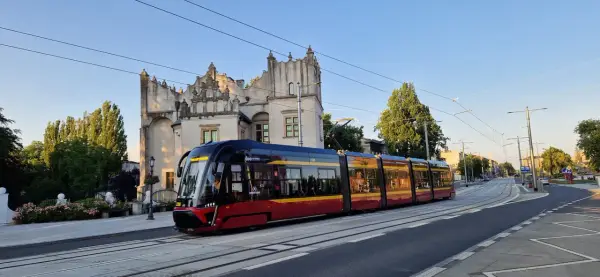 Nowoczesny tramwaj pabianice z czerwono-żółtymi pasami jedzie w stronę zabytkowego budynku.
