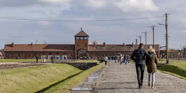 Ludzie spacerują po terenie byłego obozu Auschwitz. To miejsce pamięci, gdzie kiedyś znajdował się obóz zagłady.
