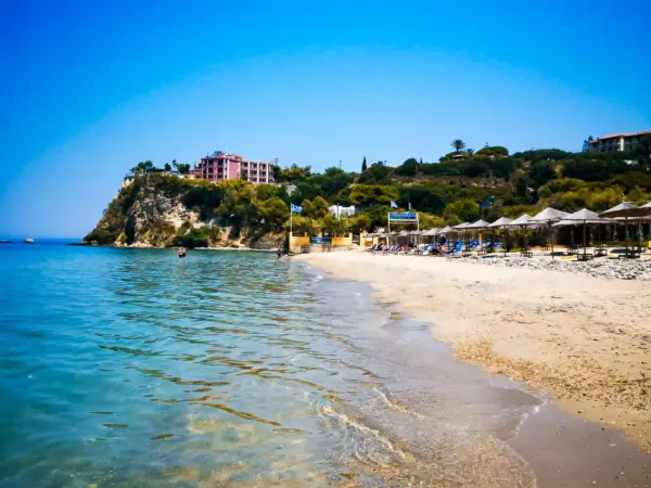 Piękne, turkusowe morze na Zakynthos. Plaża z leżakami i parasolami, a na klifie hotel.