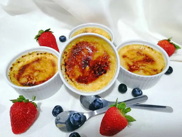 Cuatro cremosos creme brulee con una capa caramelizada, adornados con fresas y arándanos frescos.