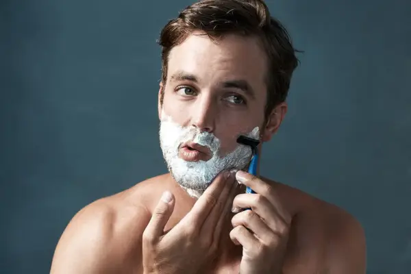 Hombre con espuma de afeitar en la cara, aprendiendo como afeitarse la barba con una maquinilla.