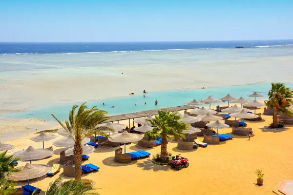 Piękna plaża z palmami i leżakami, idealna na wakacje. Wiele osób pływa w turkusowej wodzie. Blue Reef Resort opinie potwierdzają rajski wypoczynek.