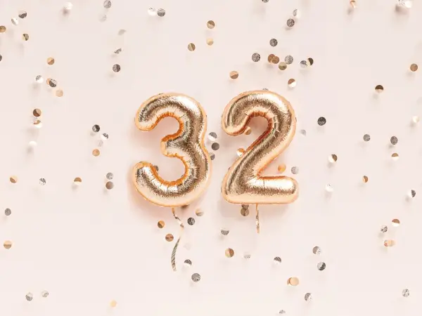 Złote balony z cyframi 3 i 2, otoczone konfetti. To już 32 tydzień ciąży, który to miesiąc?