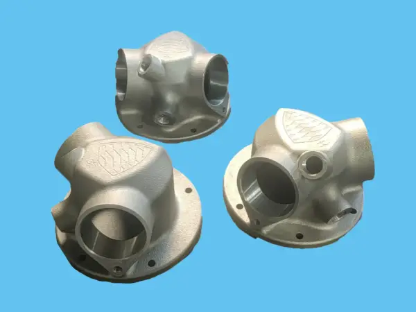 Tre componenti metallici complessi, realizzati con stampa 3D acciaio, mostrano un design intricato con diverse aperture e un logo inciso.