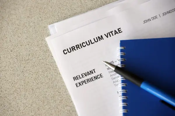 Długopis leży na dokumentach z nagłówkiem "CURRICULUM VITAE" i sekcją "RELEVANT EXPERIENCE". To klauzula CV po angielsku, gotowa do uzupełnienia.