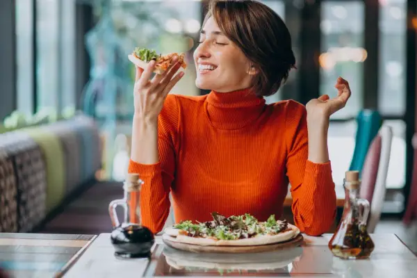 Kobieta w pomarańczowym golfie delektuje się pizzą, czując przypływ seratoniny.
