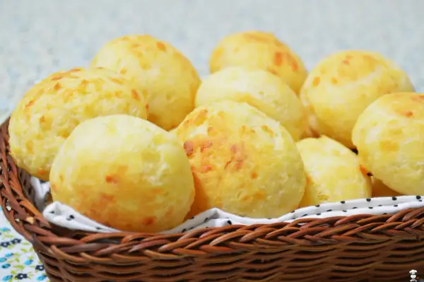 Un panier en osier déborde de délicieux pao de queijo dorés, parfaits pour un goûter.