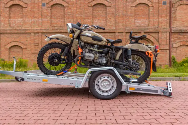 Motocykl Ural zabezpieczony pasami na przyczepie, pokazujący, jak przewieźć motocykl na zwykłej przyczepie.
