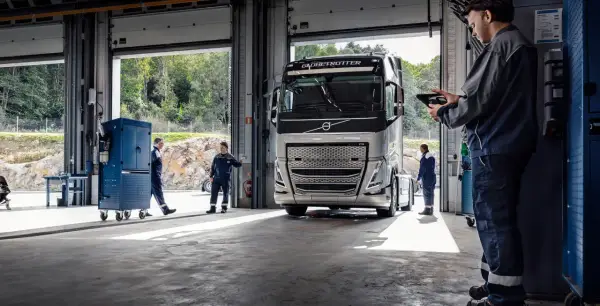 Mechanicy w serwisie obsługują nowoczesną ciężarówkę Volvo FH4. Jeden z nich sprawdza coś na tablecie.