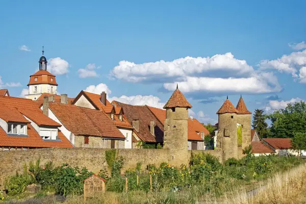 Eine malerische **Stadt im Mittelalter** mit roten Dächern, steinernen Türmen und einer alten Stadtmauer unter blauem Himmel.