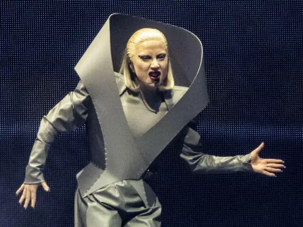 Lady Gaga w szarym, futurystycznym stroju na koncercie w Polsce, z charakterystycznym kołnierzem i makijażem.