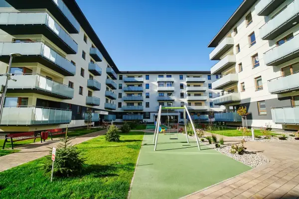 Nowoczesny **piano park** z placem zabaw i zielenią między budynkami mieszkalnymi.