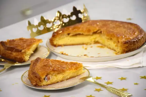 Une galette de farine dorée, prête à être dégustée, avec une fève cachée dans une part. Une couronne dorée trône à côté, promesse de fête.