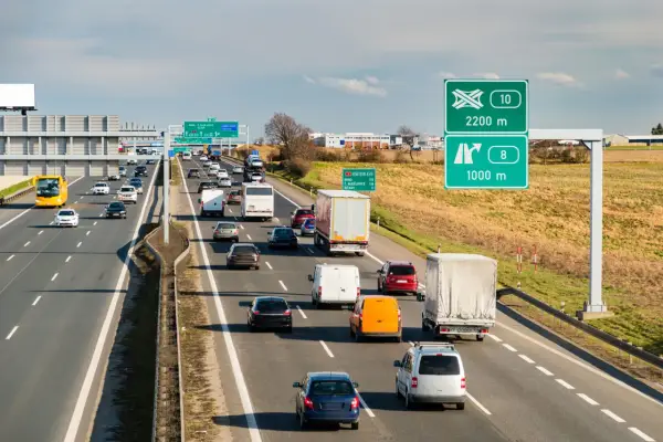 Ruch na autostradzie w Czechach, z samochodami i ciężarówkami pędzącymi z dużą prędkością. Znaki drogowe wskazują kierunki i odległości.