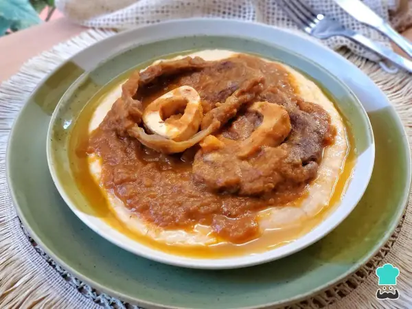 Un plato de osobuco de ternera cocinado a fuego lento, servido sobre una cama cremosa de polenta.
