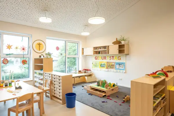 Helle, kindgerechte Reggio Raumgestaltung Kita mit Holzelementen, Spielzeug und einem Geburtstagsbanner.