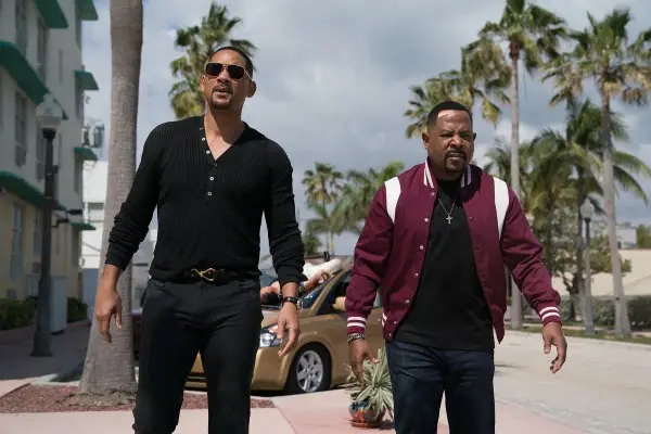 Will Smith i Martin Lawrence w filmach "Bad Boys" idą ulicą w słoneczny dzień, otoczeni palmami.
