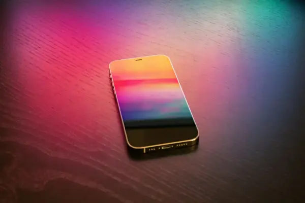 Złoty iPhone z kolorowym ekranem na drewnianym blacie. Dowiedz się, jak wgrać dzwonek na iPhone bez iTunes.