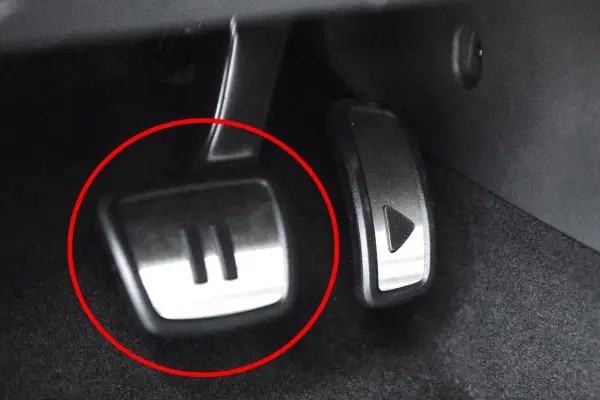 Metalowe pedały w samochodzie, jeden z symbolem "II" (auto hold) i drugi z trójkątem.