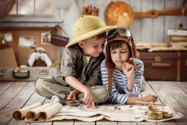 Dos niños planean una aventura en una casa rural para niños, con un mapa, lupa y sombrero de explorador.