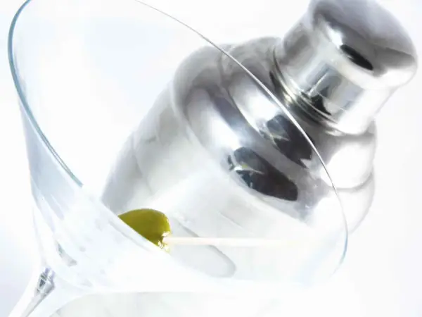 Verre à martini avec une olive, prêt pour une recette de martini gin. Shaker à cocktail en arrière-plan.