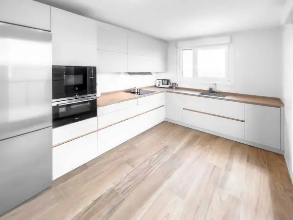 Cocina moderna con armarios blancos y encimeras de madera. El suelo de madera clara complementa perfectamente los suelos para cocinas blancas, creando un ambiente luminoso y acogedor.