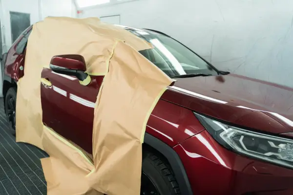 Voiture rouge bordeaux masquée pour la peinture. On se demande combien de temps entre peinture et vernis pour un tel travail.
