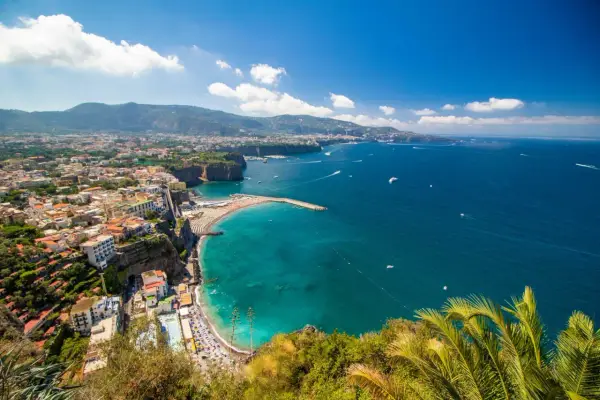 Vista panoramica della costa con il **scoglio del cavaliere** che emerge dal mare turchese, spiagge affollate e case aggrappate alla scogliera.