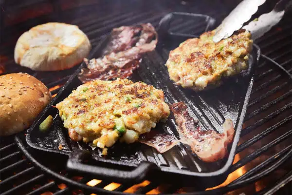 Burger-Patties und Brötchenhälften werden auf einem Grillrost zubereitet. Das Burger grillen verspricht einen köstlichen Genuss.