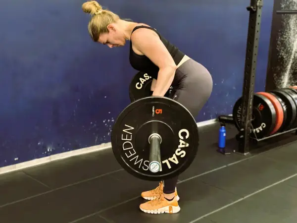 Kvinna utför en t bar row med en skivstång i ett gym.