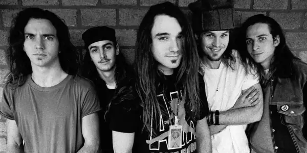Cinq membres du groupe Pearl Jam posent devant un mur de briques. L'un d'eux porte un t-shirt avec le logo du groupe.
