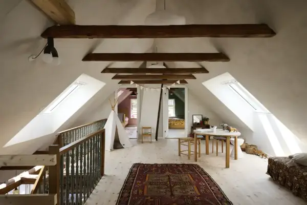 Idee per ristrutturare casa antica: mansarda luminosa con travi a vista, tappeto persiano, teepee e tavolino per bambini.