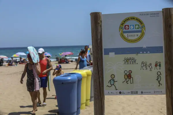 Cartel en la playa de El Carabassí, Alicante, indica "Playas sin humo". Familias disfrutan del sol y el mar.