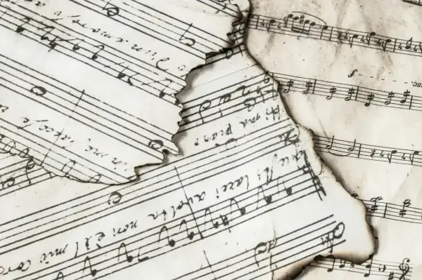 Spalone nuty z zapisem muzycznym, gdzie widać nuty i tekst. Wśród nich odnaleźć można znak bemol w muzyce, świadczący o obniżeniu dźwięku.