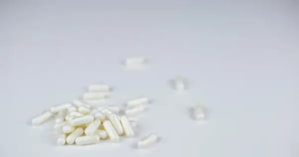 Garść białych kapsułek, jak anapran, rozsypana na białym tle. Kilka pojedynczych kapsułek leży dalej.