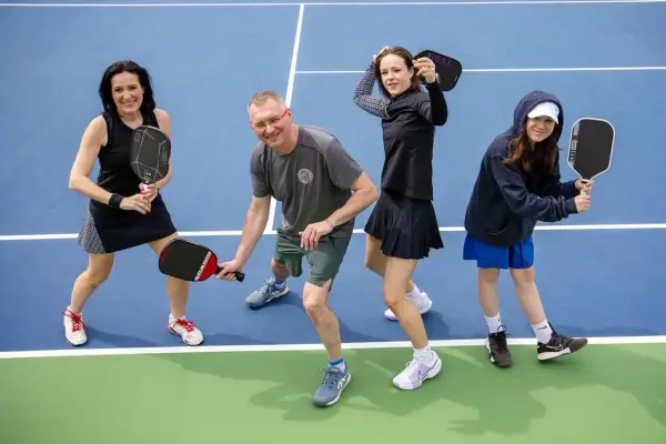 Rodzina na korcie do pickleball, co to za sport? Wszyscy trzymają rakietki, gotowi do gry.