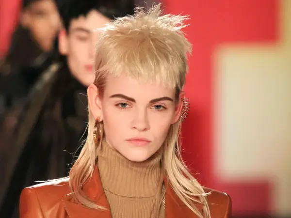 Model mit modernem Mullet-Haarschnitt, braunem Rollkragenpullover und Lederjacke. Goldene Ohrringe und auffälliger Ohrschmuck.