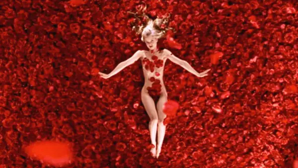 Una donna giace su un letto di rose rosse, un'immagine iconica che evoca la bellezza e la complessità di "American Beauty recensione".