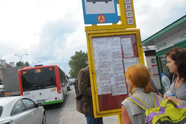Ludzie sprawdzają 79 rozkład jazdy na przystanku. Autobus linii 39 stoi obok.