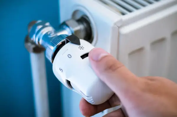 Dłoń reguluje jeden z rodzajów termostatów grzejnikowych, ustawiając temperaturę.