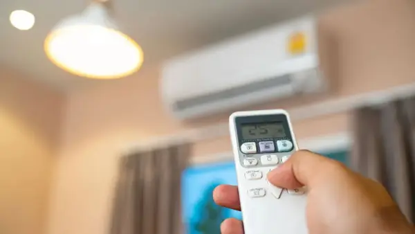 Mano sujetando control remoto para aire acondicionado, ajustando temperatura. Mantenimiento aire acondicionado para confort.