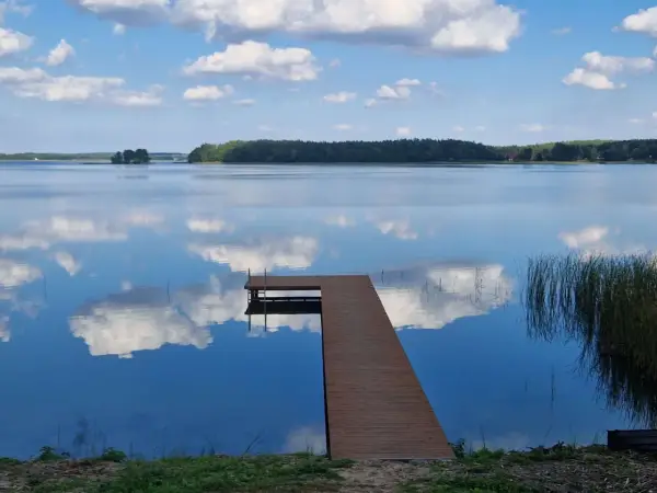 Drewniane molo na spokojnym jeziorze Wysockim, odbijającym błękitne niebo z białymi chmurami.