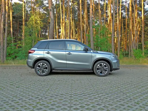 Szary Suzuki Vitara 2023 zaparkowany na tle sosnowego lasu.