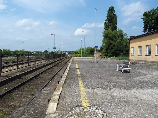 Pusta stacja kolejowa Opoczno Kielce. Torowisko, peron z ławką i żółtą linią, budynek dworca.