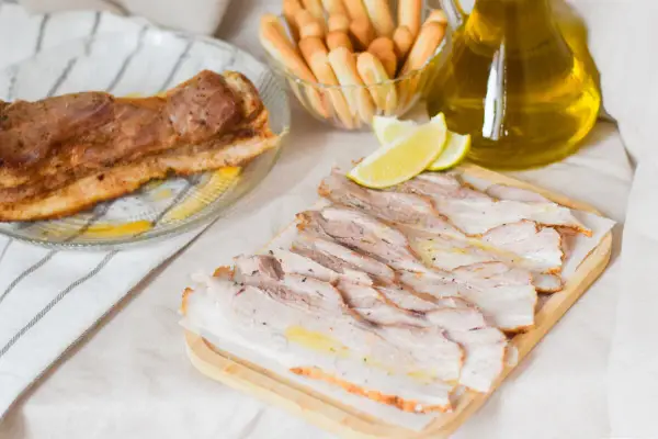 Chicharrón de Cádiz, lonchas de panceta crujiente, limones y palitos de pan, listos para disfrutar.