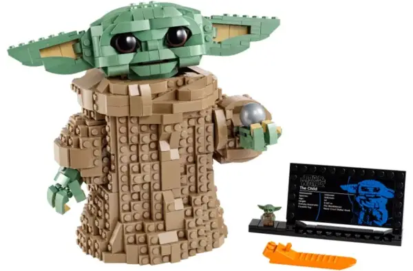 Figurka Grogu z klocków LEGO, znana z gier LEGO Star Wars, trzyma srebrną kulę. Obok stoi mała figurka i tabliczka informacyjna.