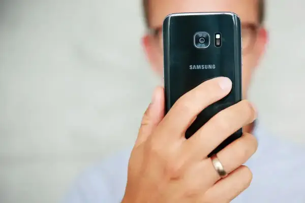 Osoba trzyma czarny telefon Samsung, pokazując tył z aparatem. Dowiedz się, jak poprawić jakość aparatu w telefonie Samsung, aby robić lepsze zdjęcia.