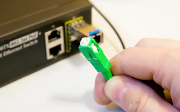 Zielona wtyczka światłowodu gotowa do podłączenia do switcha w bloku. Szybki internet w zasięgu ręki.