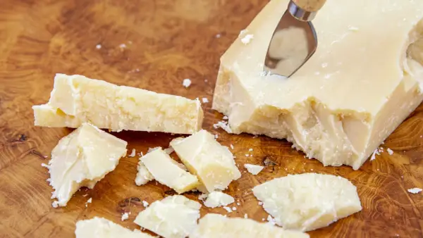 Kawałki Grana Padano na drewnianej desce, gotowe do posypania makaronu lub dodania do sosów.